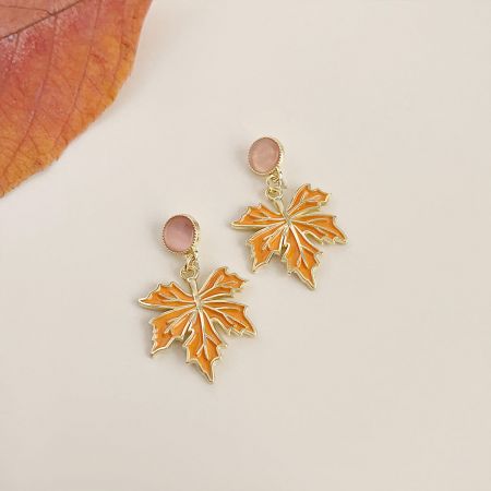 Close-up dos brincos de folha de bordo em esmalte laranja com ricos detalhes em ouro.