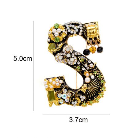 El broche ornamentado de la letra 'S', que presenta un diseño lujoso con joyas brillantes y elegantes perlas.