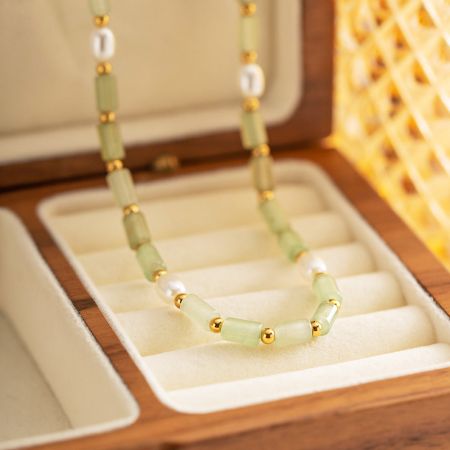 Un collar de cuentas verde pálido con separadores de oro, exhibido elegantemente en una caja de joyería de madera.