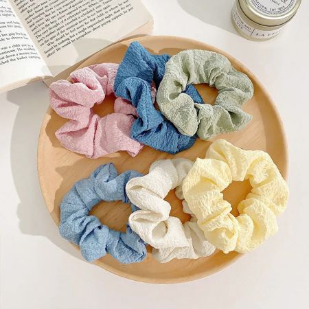 Um conjunto de seis scrunchies em cores pastel elegantemente dispostos em um prato de madeira rústica.
