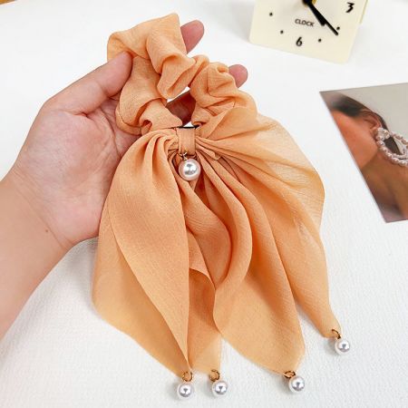 Detailed view of a peach silk scrunchie adorned with delicate pearl accents.