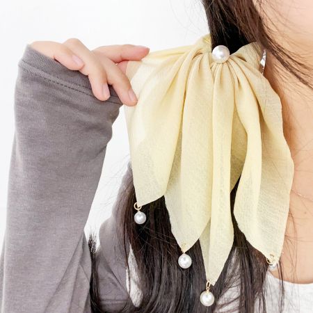 Close-up of a hair scrunchie featuring a bow design and pearl accents.