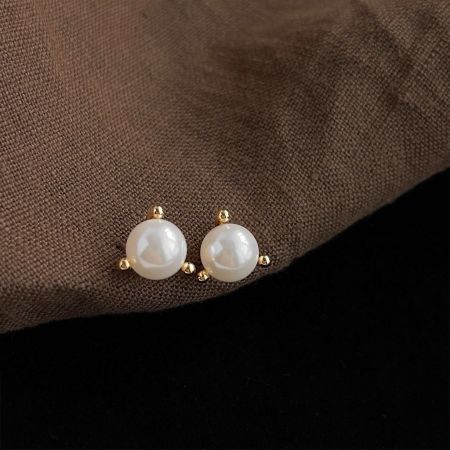Detailed view of the gold settings on the simple pearl stud earrings.