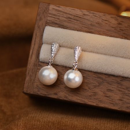 Orecchini a Pendente in Argento Sterling 925 con Perle - Un paio di eleganti orecchini a pendente in argento sterling 925 con perle e punte in zirconia cubica scintillante, esposti in una scatola di gioielli in legno.