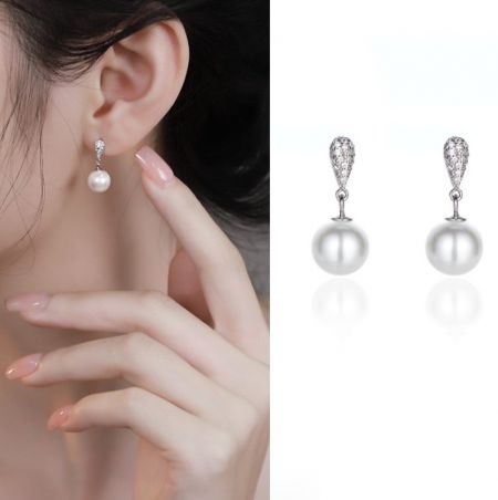 Primo piano degli orecchini a pendente in argento sterling 925 con perle che mostrano l'intricato montaggio in argento e le brillanti pietre.