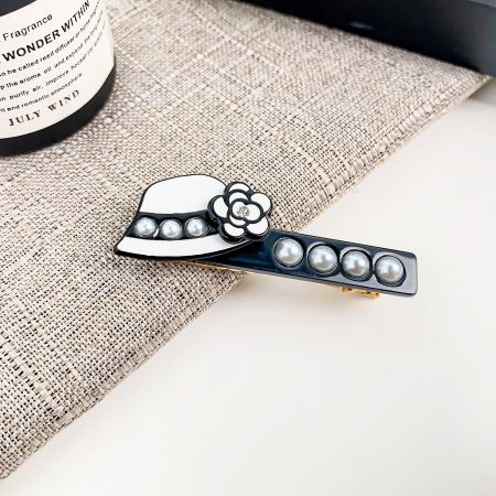 Primo piano di una clip per capelli a forma di cappello unica in bianco, adornata con un delicato fiore e perle lucenti.