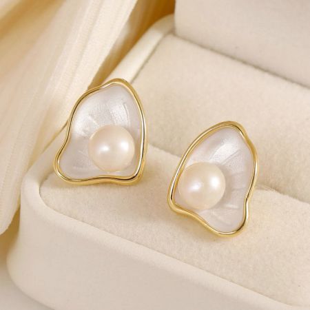 A pair of white enamel scallop pearl earrings presented in a cream-colored jewelry box.