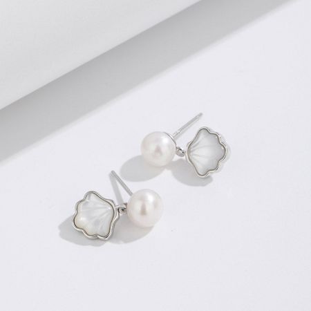 Ein Paar Ohrringe aus Sterlingsilber mit Muschel und Perle, das die glänzenden Materialien hervorhebt.