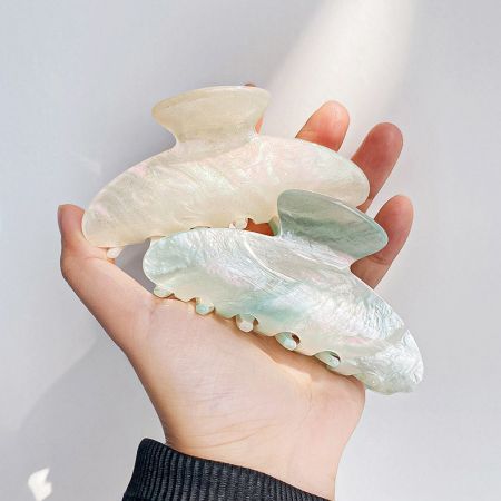 A hand holding two pearlescent hair clips to show their size and design.