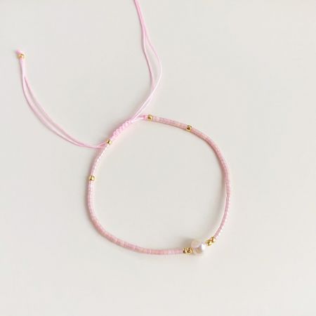 Un affascinante braccialetto rosa con perline e dettagli dorati, con una perla centrale, perfetto per essere impilato.
