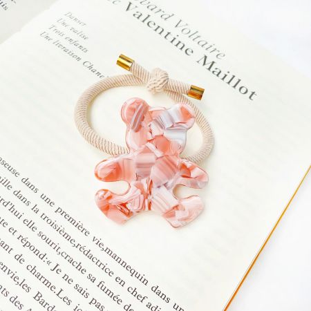 Detailed view of a single pink and white marbled acetate bear charm on a beige elastic hair tie.