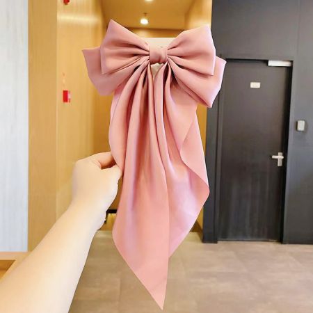 Um prendedor de cabelo em forma de laço de cauda longa rosa suave, perfeito para um look delicado.