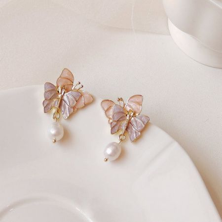Charmantes boucles d'oreilles pendantes en émail rose en forme de papillon accentuées de perles d'eau douce.