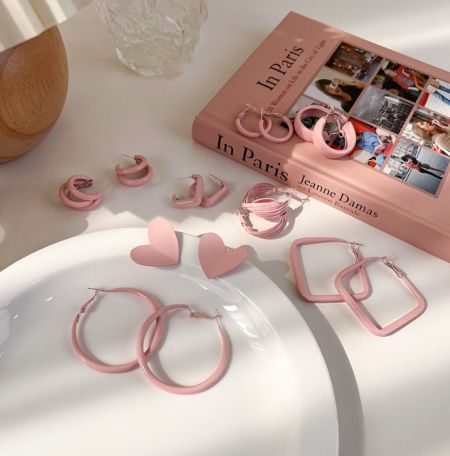 Pink enamel earrings artfully arranged next to a book about Paris, evoking a chic and fashionable vibe.