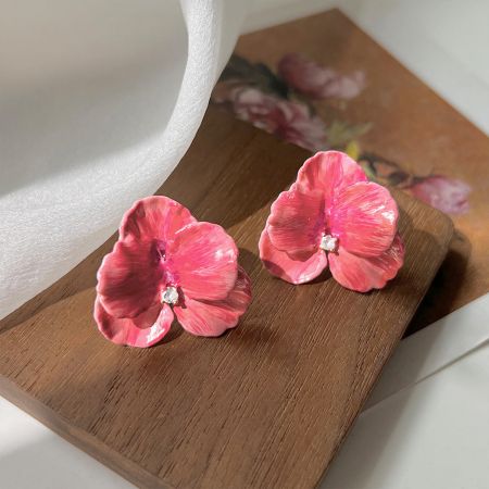白い背景にある宝石の中心を持つ光沢のあるピンクの花イヤリングのペア。