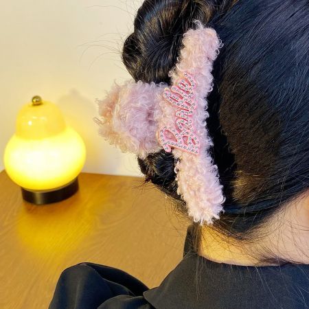 Um fofo clipe de cabelo peludo rosa com a palavra 'beijo' em uma fonte divertida.