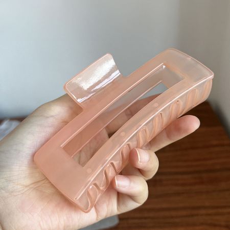 Close-up of a pink rectangle hair claw clip held in hand, showing its curved design.