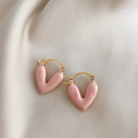 The pink enamel heart hoop earrings displayed on a textured fabric background.