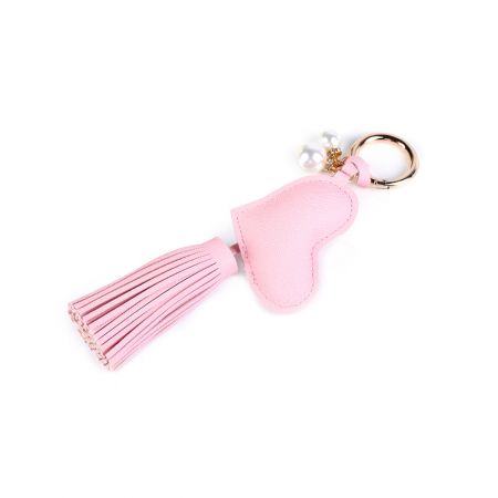 Detailansicht des rosa, herzförmigen Schlüsselanhängers aus PU-Leder, mit einer weichen Quaste und zarten Perlenakzenten.