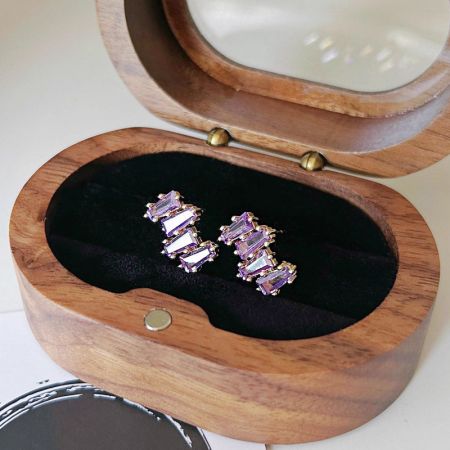 Un paio di orecchini in pietra viola elegantemente presentati in una scatola di gioielli in legno.