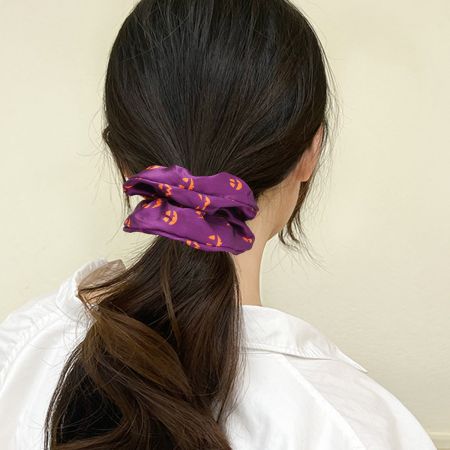 A model wearing a purple Halloween scrunchie with orange jack-o'-lanterns in a low ponytail.