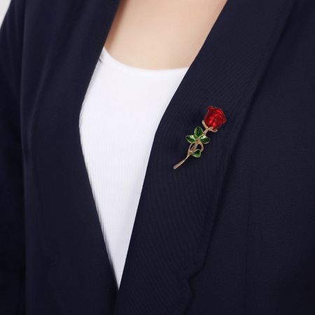 Joyería de Vestido para Mujeres Metal Esmalte Broche de Flor de Rosa 3D - Un broche de flor de rosa de esmalte rojo bellamente elaborado con un tallo de oro, elegantemente sujeto en la solapa de un blazer oscuro.