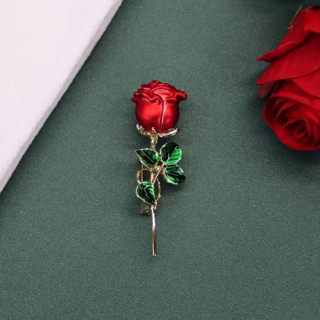 Gedetailleerd uitzicht op de rode rozenbroche, met de levendige emaille en groene bladvormen.