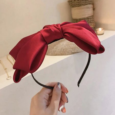 Una diadema de satén rojo vibrante con un gran lazo elegante sostenida en la mano.