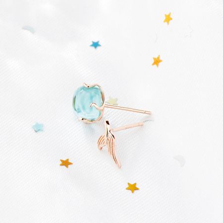 Rose gold variant of the mermaid fishtail stud earring with a light blue gemstone.
