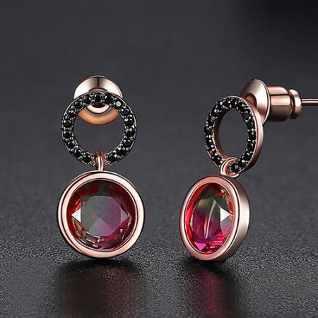 Un autre angle des boucles d'oreilles en or rose, soulignant le contraste entre le verre rouge et le zircon cubique noir.