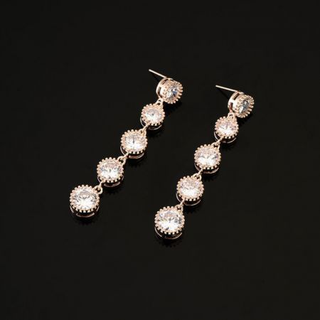 Gros plan des élégantes boucles d'oreilles longues en strass pour mariée, soulignant l'éclat des cristaux blancs contre le plaquage en or rose.