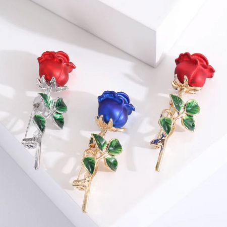 Verzameling van drie 3D rozenbloem broches in rode, blauwe en vergulde afwerkingen.