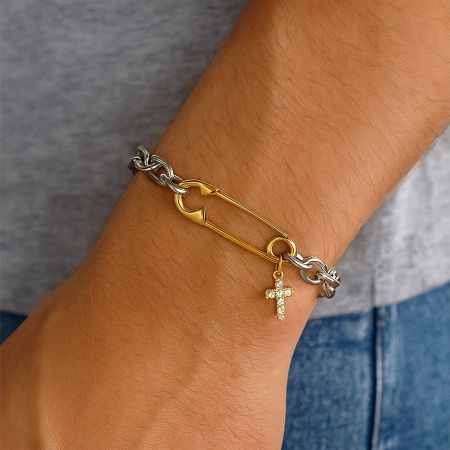 Detaljerad närbild av det zirkonbesatta korscharmet och säkerhetsnålslänken på armbandet i rostfritt stål.