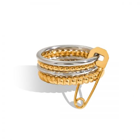 Conjunto de anillos apilables de oro y plata con charm de imperdible - Un primer plano de un conjunto único de anillos apilables con un diseño de oro y plata con un prominente charm de imperdible, hecho de acero inoxidable que no se empaña.