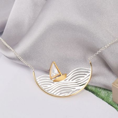 Collar con colgante de velero de ola móvil de plata esterlina 925 - Un primer plano detallado del colgante de velero de plata esterlina 925, mostrando su intrincado diseño de ola y vela de nácar en una cadena de color dorado.