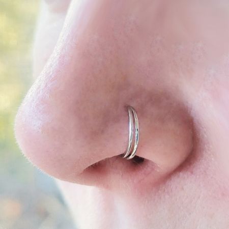 Una vista della gioielleria nasale a doppio anello indossata come piercing al setto, dimostrando la sua versatilità.
