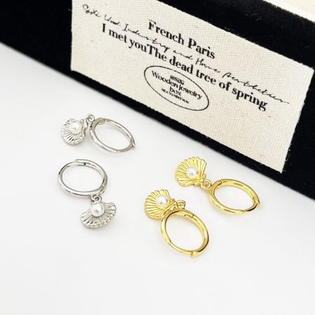 Entrambi gli orecchini a conchiglia con perla in oro e argento elegantemente esposti accanto a una scatola di gioielli in legno.