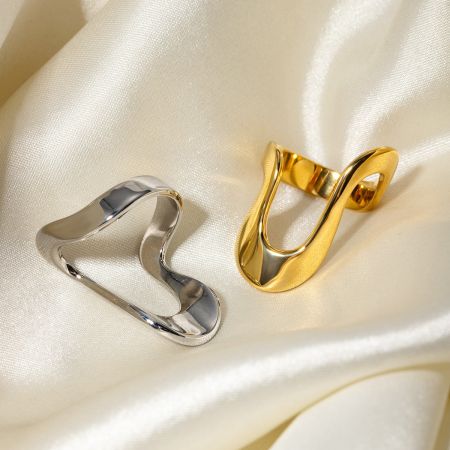Anelli in acciaio inossidabile con design geometrico irregolare - Set di 5 - Un set di anelli geometrici in acciaio inossidabile, con un anello in argento e uno in oro con un design ad infinito aperto, esposti su uno sfondo bianco.