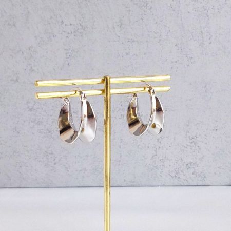 Gli orecchini a cerchio ondulati in argento esposti elegantemente su un supporto dorato.