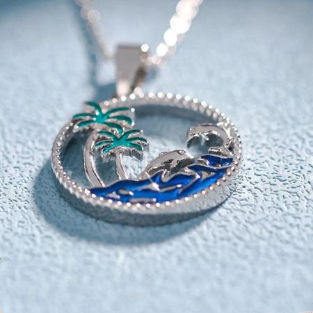 Detailed view of a silver pendant with a beach scene, including a palm tree and an animal figure.