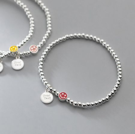 Vista ravvicinata di due braccialetti in argento sterling con perline, uno con un ciondolo a forma di faccina sorridente gialla.