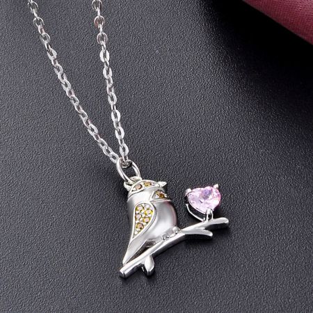 Detailed shot of the sparrow bird pendant, highlighting the intricate branch design and the vibrant pink heart-shaped gemstone.