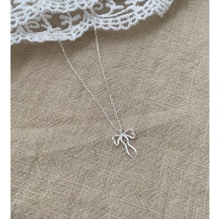 Detailed shot of the silver bow pendant on a textured fabric, showing its fine craftsmanship.