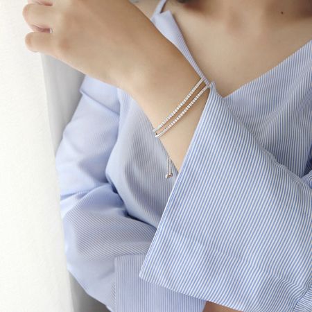 Ein Modell trägt das stapelbare doppellagige CZ-Tennisarmband und zeigt seinen eleganten Stil mit einem weißen Outfit.