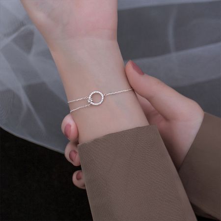 925 Sterling Zilver Asymmetrische Ketting Zircon Geometrische Armband - Een close-up van een 925 sterling zilveren armband met een asymmetrische ketting en een geometrische ronde charme bezet met sprankelende zirconia stenen.