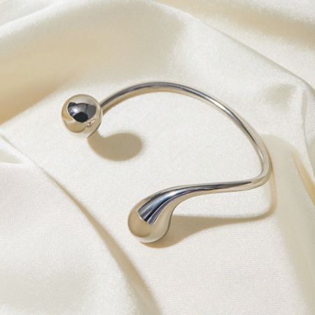 Zijprofiel van de zilveren cuff bangle, met de bolvormige bal en druppelvormige uiteinden.