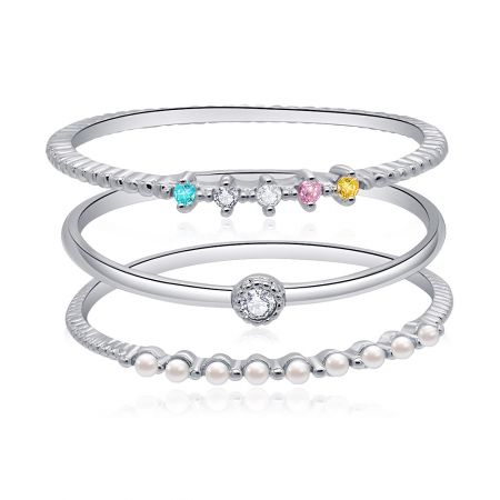 Conjunto de anillos de banda apilables ultra delgados de 3 piezas. - Un conjunto de tres anillos de banda apilables ultra delgados con piedras de circonita cúbica de varios colores, exhibidos sobre un fondo neutro.