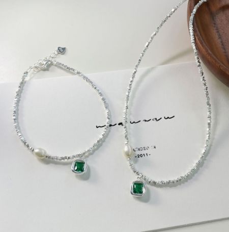 Un par de pulseras de perlas y esmeraldas de plata esterlina 925 exhibidas sobre una superficie blanca, destacando los intrincados detalles de las piedras preciosas verdes y las perlas.