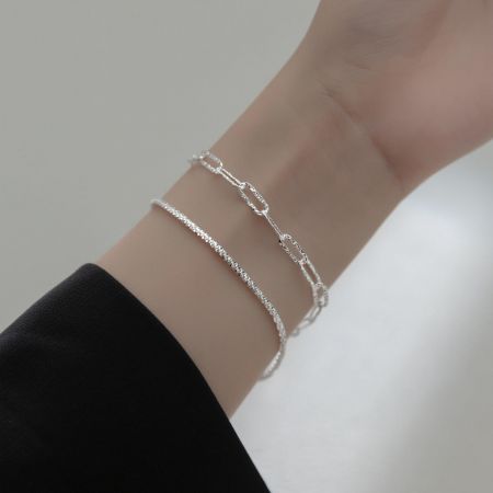 Vista detalhada das pulseiras de corrente de clipe de papel prateadas empilhadas em um pulso.