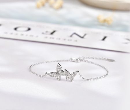 Vista detallada del charm de mariposa de plata, incrustado con piedras de circonio brillantes.